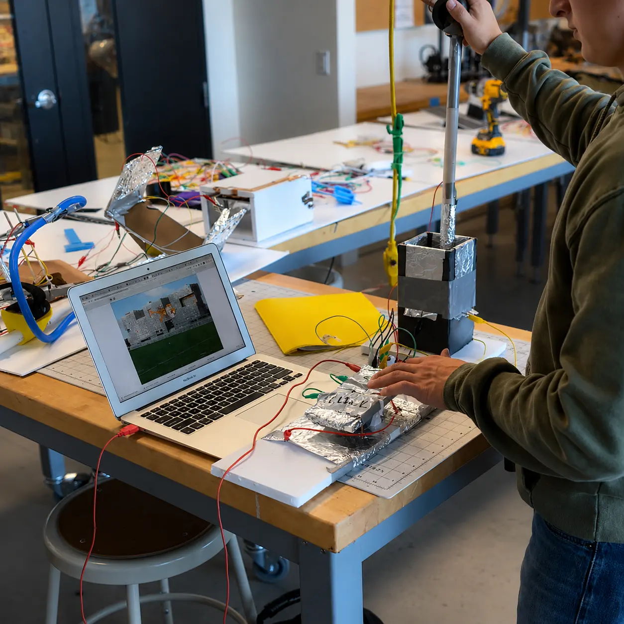 A maker using a flat foil-and-tape adaptive game controller on a workbench next to a laptop