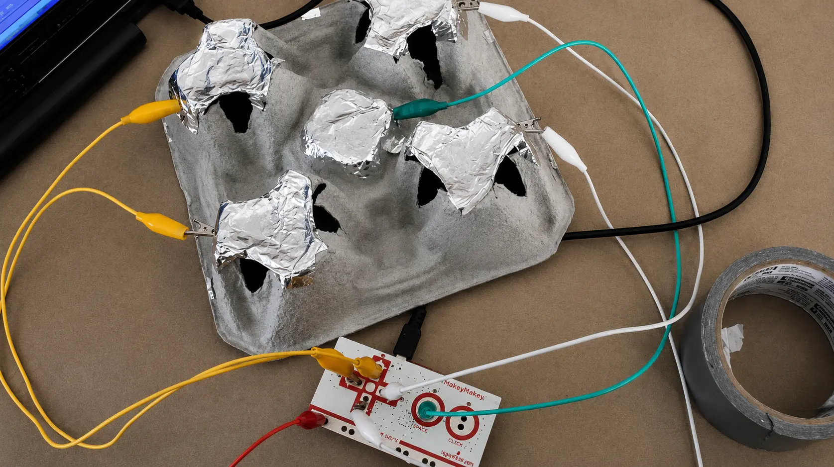 An egg carton lined with aluminum foil and clipped with alligator clips to a Makey Makey board