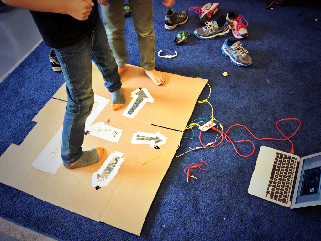 Students standing on a cardboard floor controller with taped arrow keys